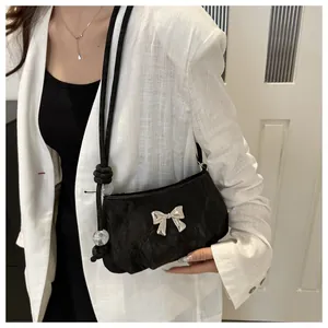 Detail of a black crossbody bag with silver butterfly buckle and beaded strap
