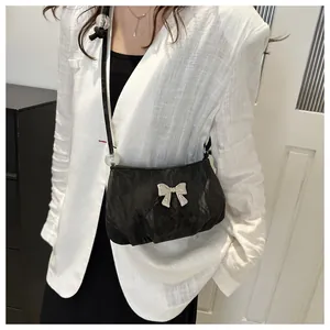 Detail of black pleated crossbody bag featuring a silver butterfly buckle on white blazer