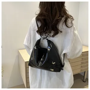 Detail showing high-shine black leather tote bag with metallic silver butterfly ornaments