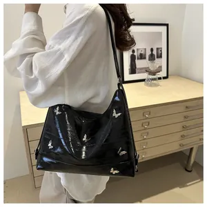 Glossy black tote bag with silver butterfly metal accents worn on a shoulder