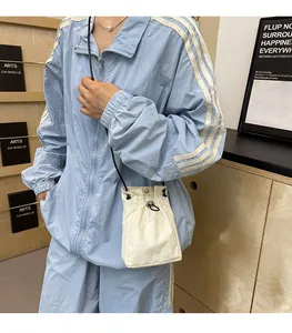 Detail view of a cream nylon drawstring bucket bag paired with a light blue zip-up jacket