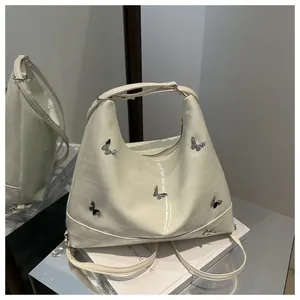 Detail of white crocodile pattern handbag with silver butterfly hardware accents