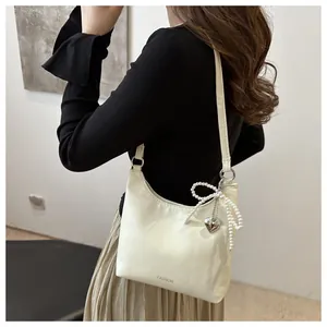 Détail du sac hobo crème avec breloque nœud en perles et lettrage fashion embossé