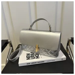 Détail d'un sac argenté avec surpiqûres matelassées et fermoir rotatif doré en métal brillant