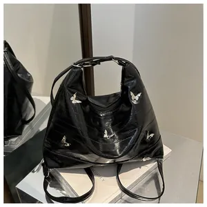 Detail of black glossy tote bag featuring quilted texture and silver butterfly hardware