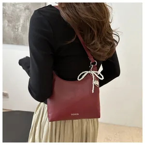 Détail du sac bandoulière bordeaux avec nœud en perles et pendentif cœur argenté