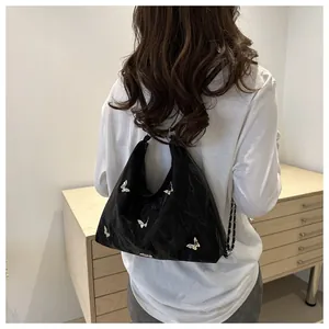 Detail of black pleated shoulder bag featuring a 3D silver butterfly and chain strap
