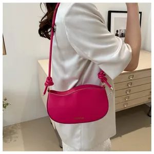 Detail of a magenta crescent shoulder bag with knotted strap and gold hardware accents