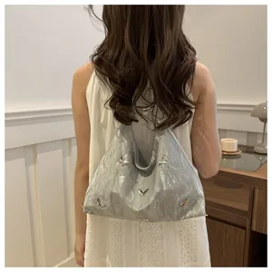 Detail of silver-grey tote bag with pleated texture and metallic butterfly accents