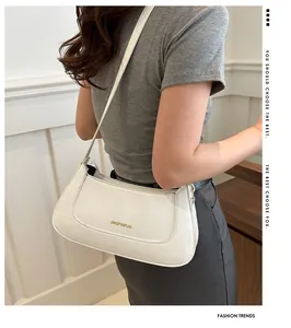Side view of a minimalist cream white faux leather crescent bag worn by a model