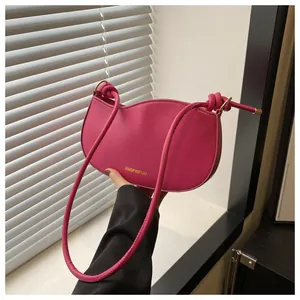Detail of rose red crescent bag with knotted shoulder strap and gold hardware accents