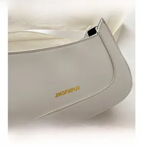 Detail of white faux leather shoulder bag with gold embossed logo and fine stitching
