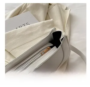 Close-up of a smooth gold metal zipper on a white minimalist square shoulder bag