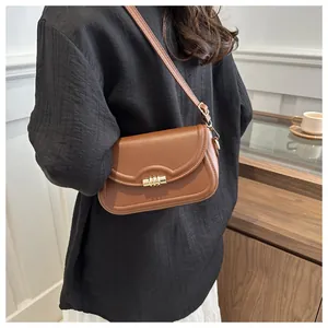 Brown leather crossbody bag with wave-edge flap and golden metal clasp shown on model