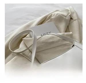 Detail of white leather shoulder bag with logo on elegant beige textured blazer