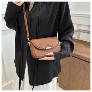 Close-up of brown leather crossbody bag with gold cylindrical lock on black shirt and white skirt