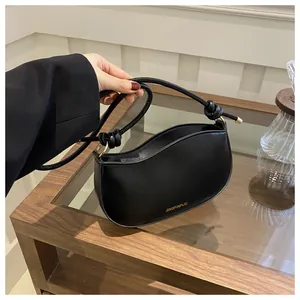 Detail of black bow shoulder bag with elegant matte texture and knot hardware on wood table