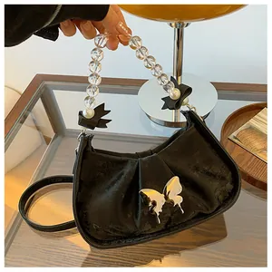 Détail d'un sac à main en velours noir avec fermoir papillon en métal et anse en perles