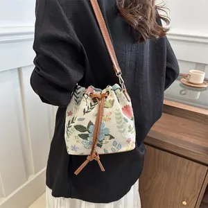 Detail of floral tapestry bucket bag with brown leather strap and drawstring closure