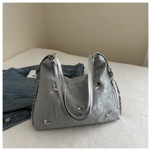 Macro shot of silver textured shoulder bag featuring metallic butterfly charms and chain details