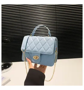 Detail of light blue quilted mini bag with gold chain strap held by hand for size context