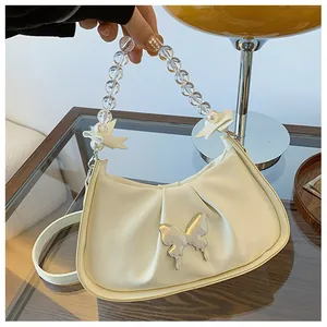 Détail du sac beige plissé avec papillon argenté et bandoulière en perles élégante