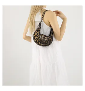 Detail of leopard print crescent bag with golden clasp on white pleated dress