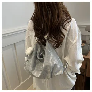 Silver metallic pleated tote bag shown on shoulder with soft white plush pendant detail