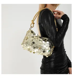 Detail of gold sequin shoulder bag with knot handle worn by model in black dress
