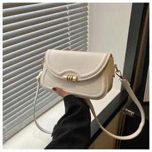 Detail view of a white minimalist crossbody bag with elegant gold cylindrical buckle