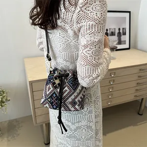 Ethnic style woven bucket bag with geometric patterns and leather strap worn by a model