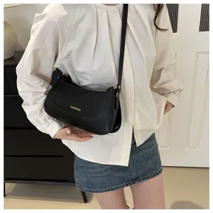 Close-up of matte black faux leather shoulder bag with gold logo on white shirt