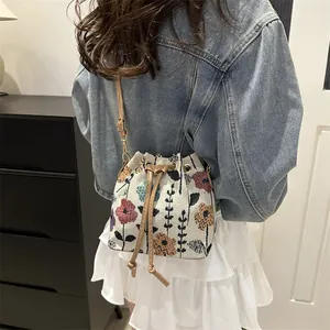 Detail of floral embroidery bucket bag with drawstring closure and leather strap