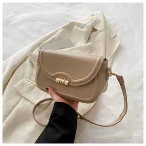 Detail of beige flap bag featuring a cylindrical gold clasp and smooth faux leather