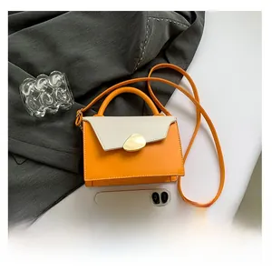 Detail view of stylish orange and beige handbag with gold clasp beside a smartphone