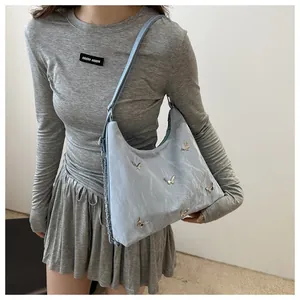 Detail of light blue textured shoulder bag with silver butterfly charms and chain strap