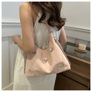Pink shoulder bag with silver butterfly charms and chain strap shown on model in a room