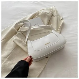 Close-up of minimalist white leather underarm bag with gold logo and shoulder strap