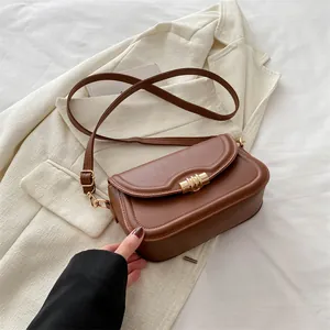 Elegant brown PU leather crossbody square bag with gold lock on a beige blazer background