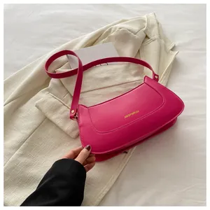 Detail of fuchsia PU leather baguette bag featuring gold lettering and wide shoulder strap