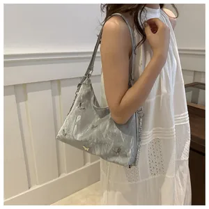 Detail of silver metallic wrinkled shoulder bag featuring a 3D butterfly metal ornament