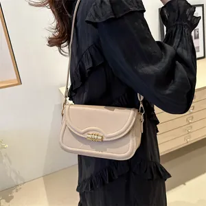 Elegant beige crossbody bag with wavy flap and gold buckle on a model in a cozy room