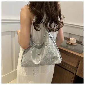 Silver shoulder bag with metallic pleats and butterfly accents worn by a model