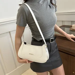 Minimalist white leather underarm bag with gold logo shown in a lifestyle setting