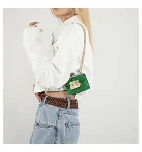 Petit sac bandoulière vert avec chaîne dorée porté par un mannequin en veste blanche