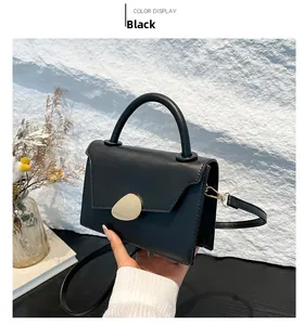 Detail of black PU leather handbag featuring a golden buckle and round handle on white wall