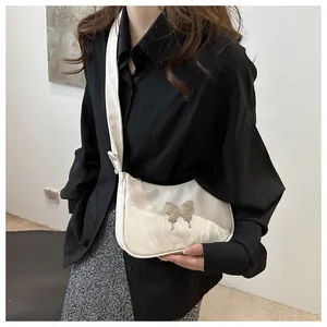 Detail of white half-moon bag with silver butterfly accent and satin texture strap