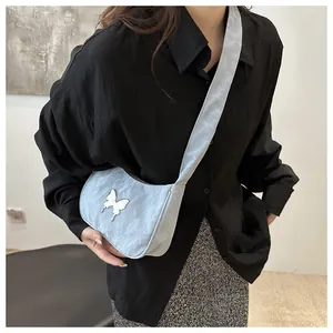Detail of light blue pleated bag featuring a silver metal butterfly and wide shoulder strap