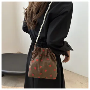 Détail du sac seau en velours fraise avec bandoulière en perles porté par un mannequin