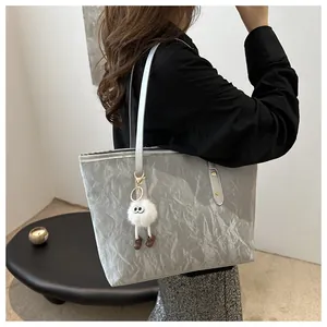 Detail of grey wrinkled metallic tote bag with cute monster plush charm on shoulder